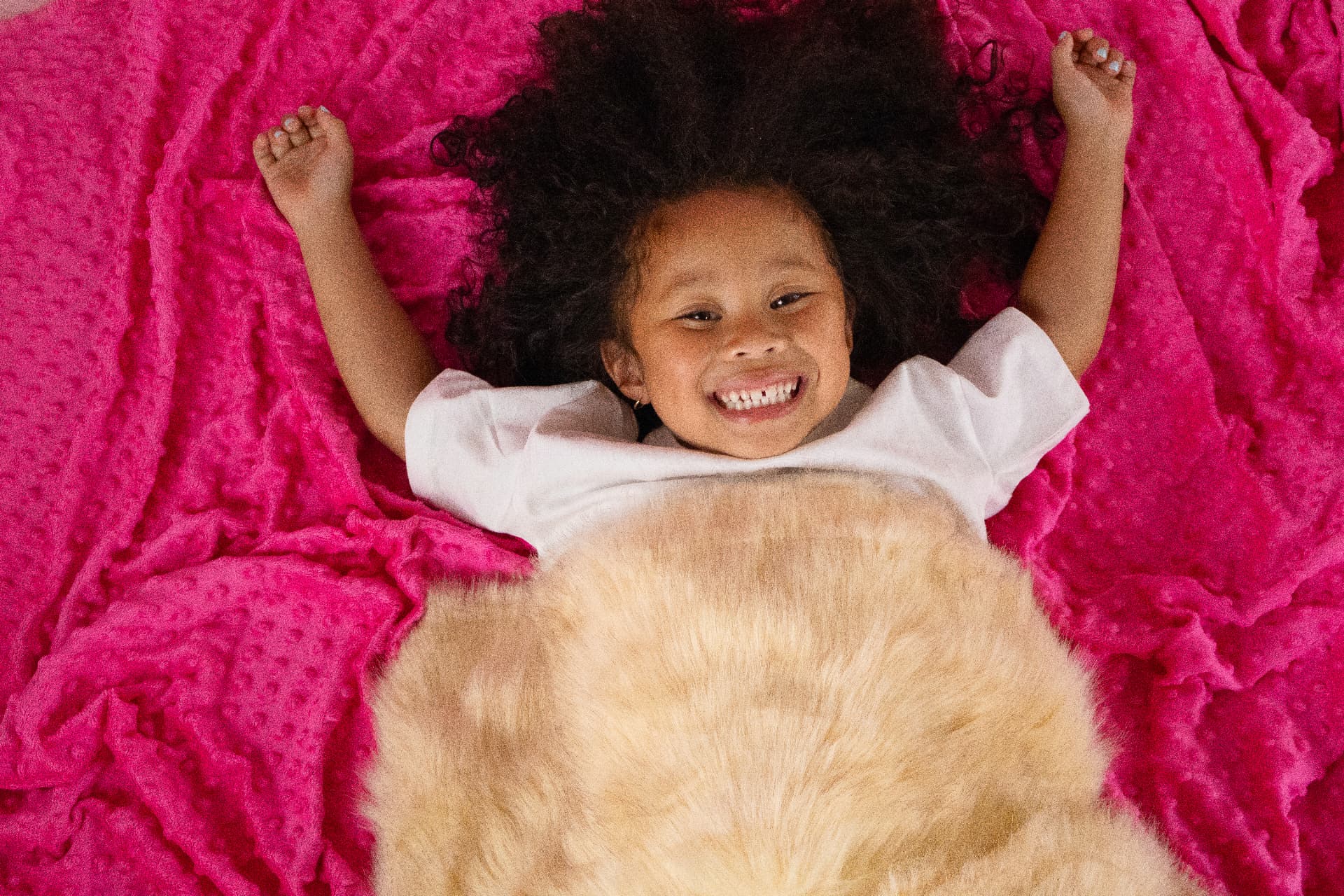Milani laughing on a bright pink blanket with her arms raised