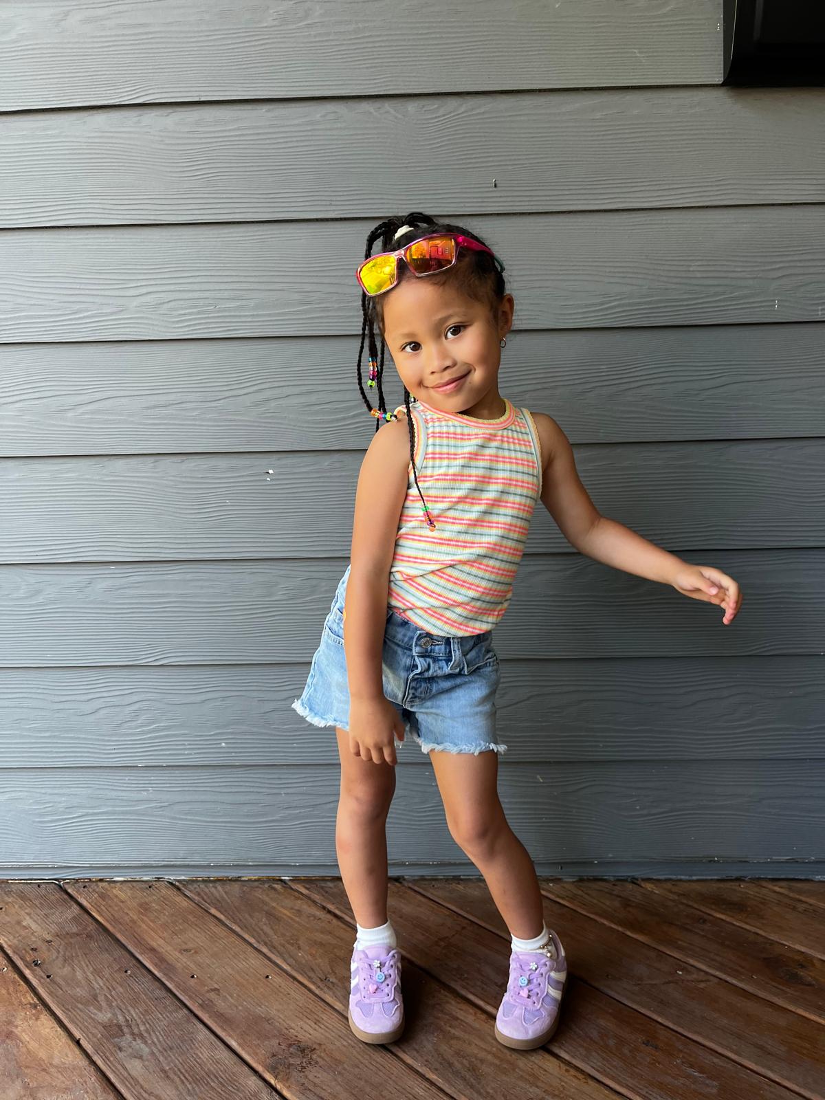 Milani in a rainbow striped tank and denim shorts with beaded braids