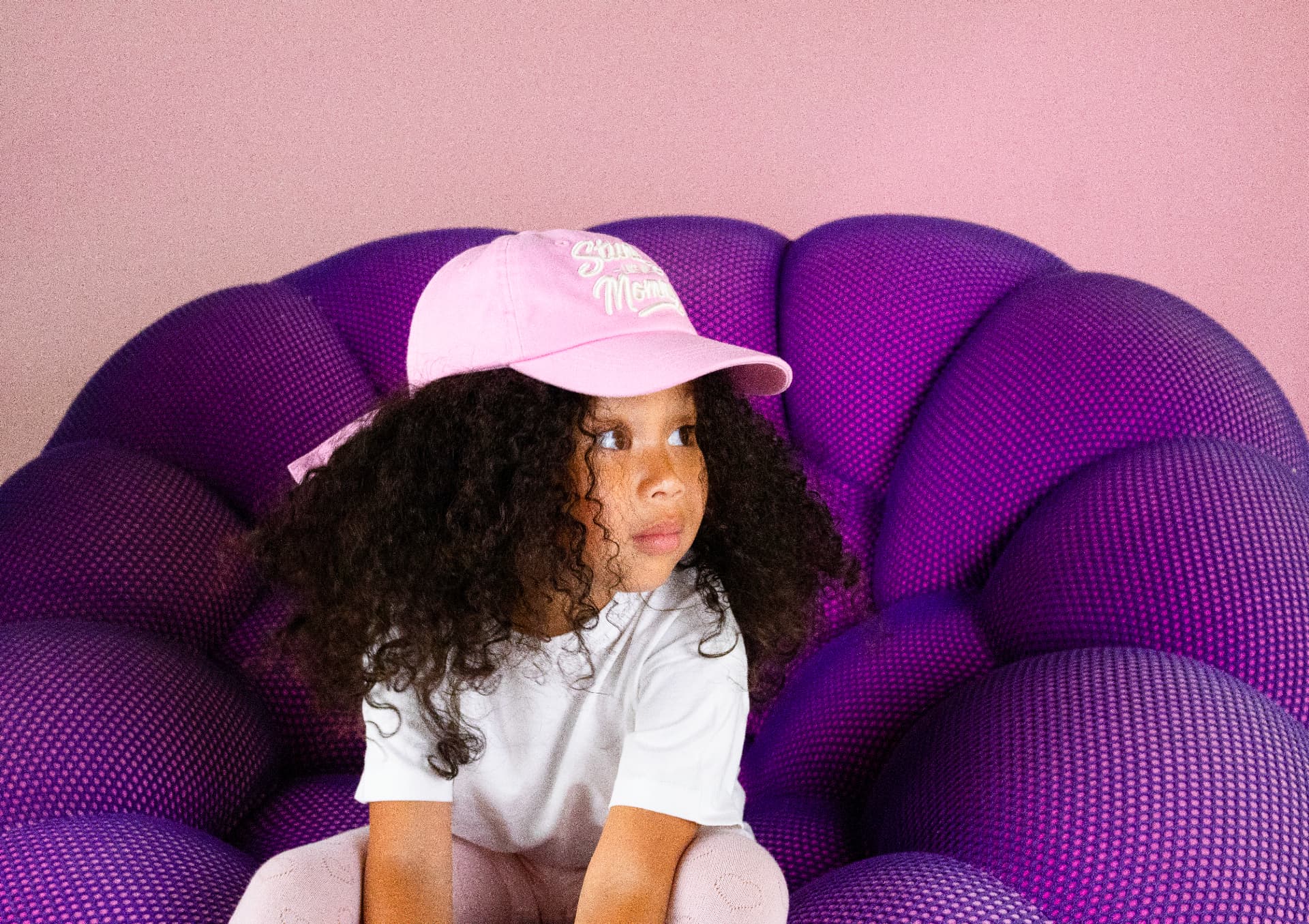 Milani seated in a sculptural purple chair wearing a pink cap and white polo shirt