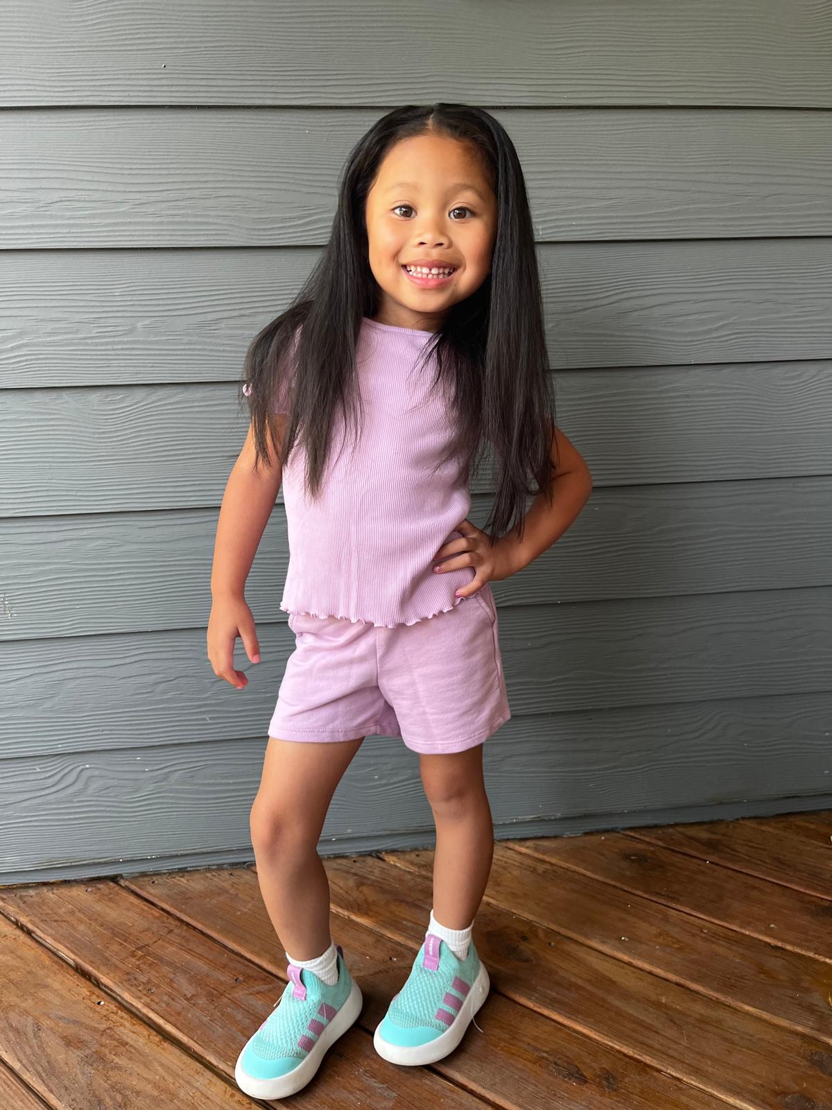 Milani smiling in a lavender ribbed top and matching shorts