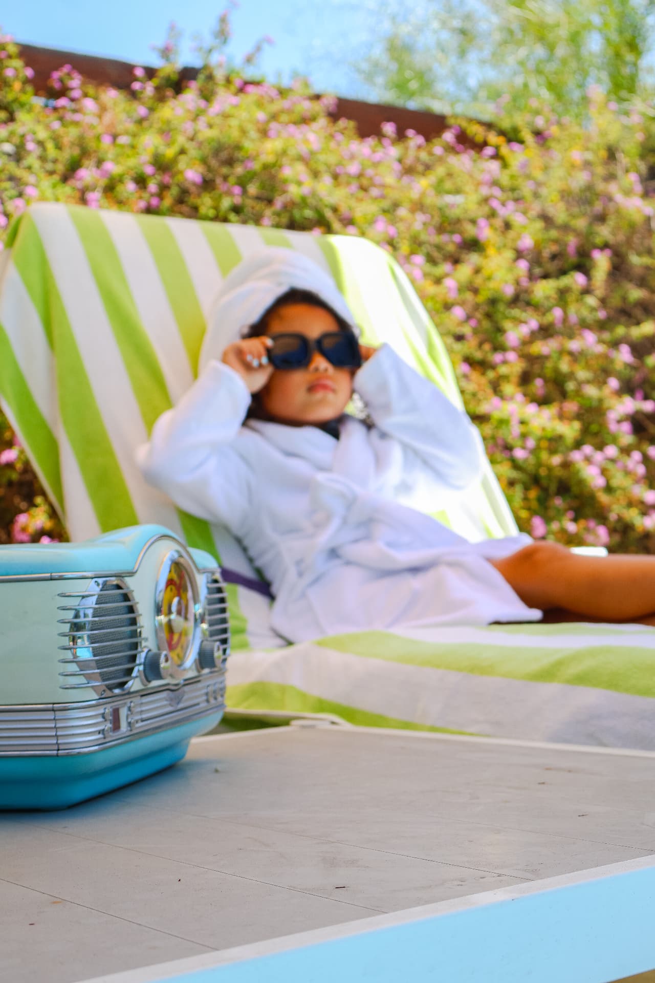 Milani relaxing in a white robe and sunglasses beside a retro blue radio