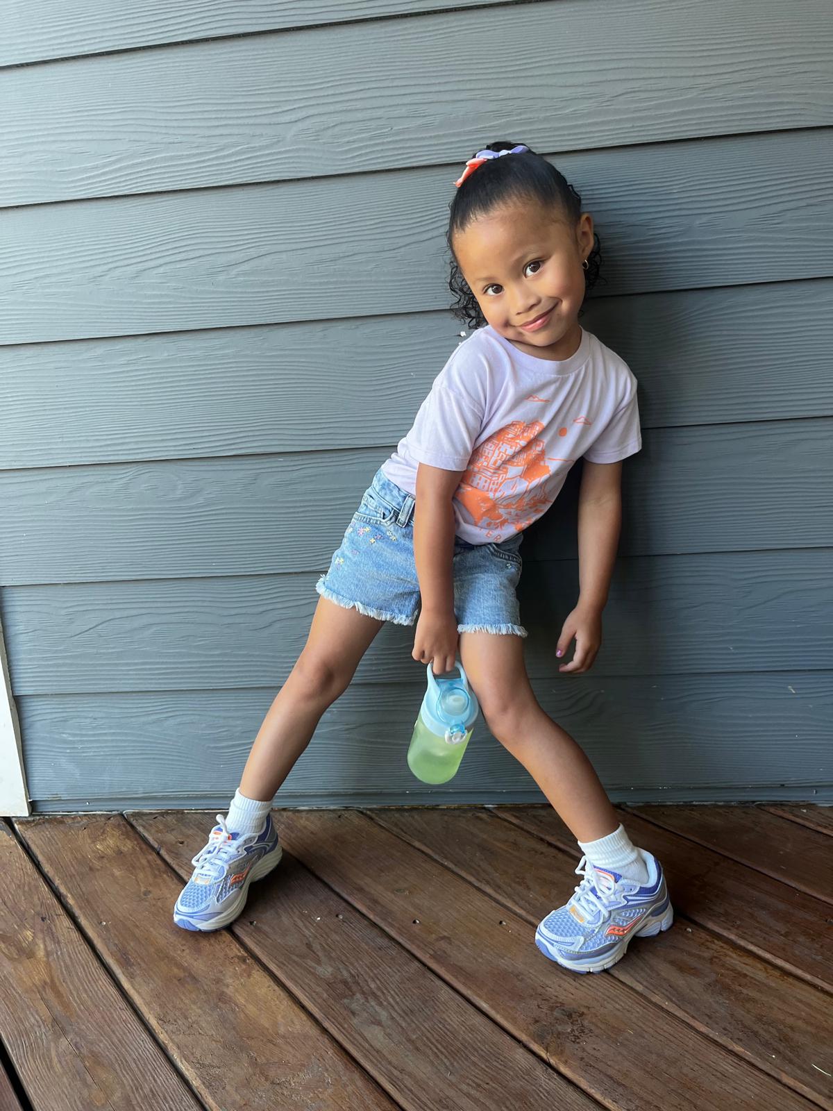 Milani in a white graphic tee and denim shorts, full-length porch portrait